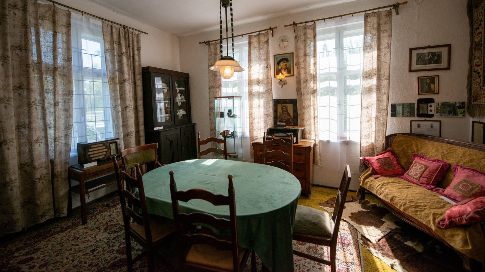 Salon z kanapą, stołem nakrytym zielonym obrusem i obrazami w Muzeum Historyczno-Etnograficznym w Andrychowie