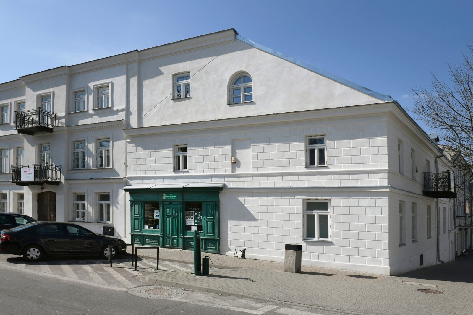 Biały narożny budynek Muzeum Ziemi Chełmskiej z zieloną witryną w Chełmie