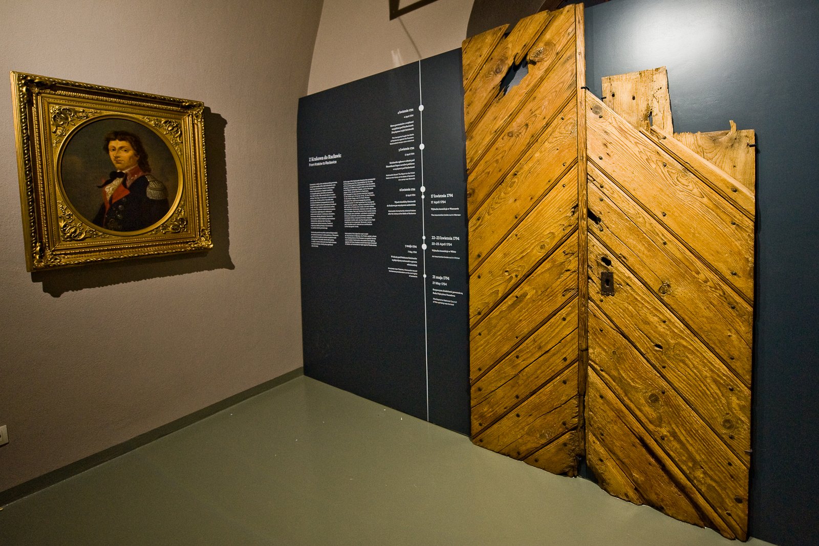 Portret Tadeusza Kościuszki w złoconej ramie i stare drewniane drzwi na wystawie Muzeum Kościuszkowskiego w Krakowie