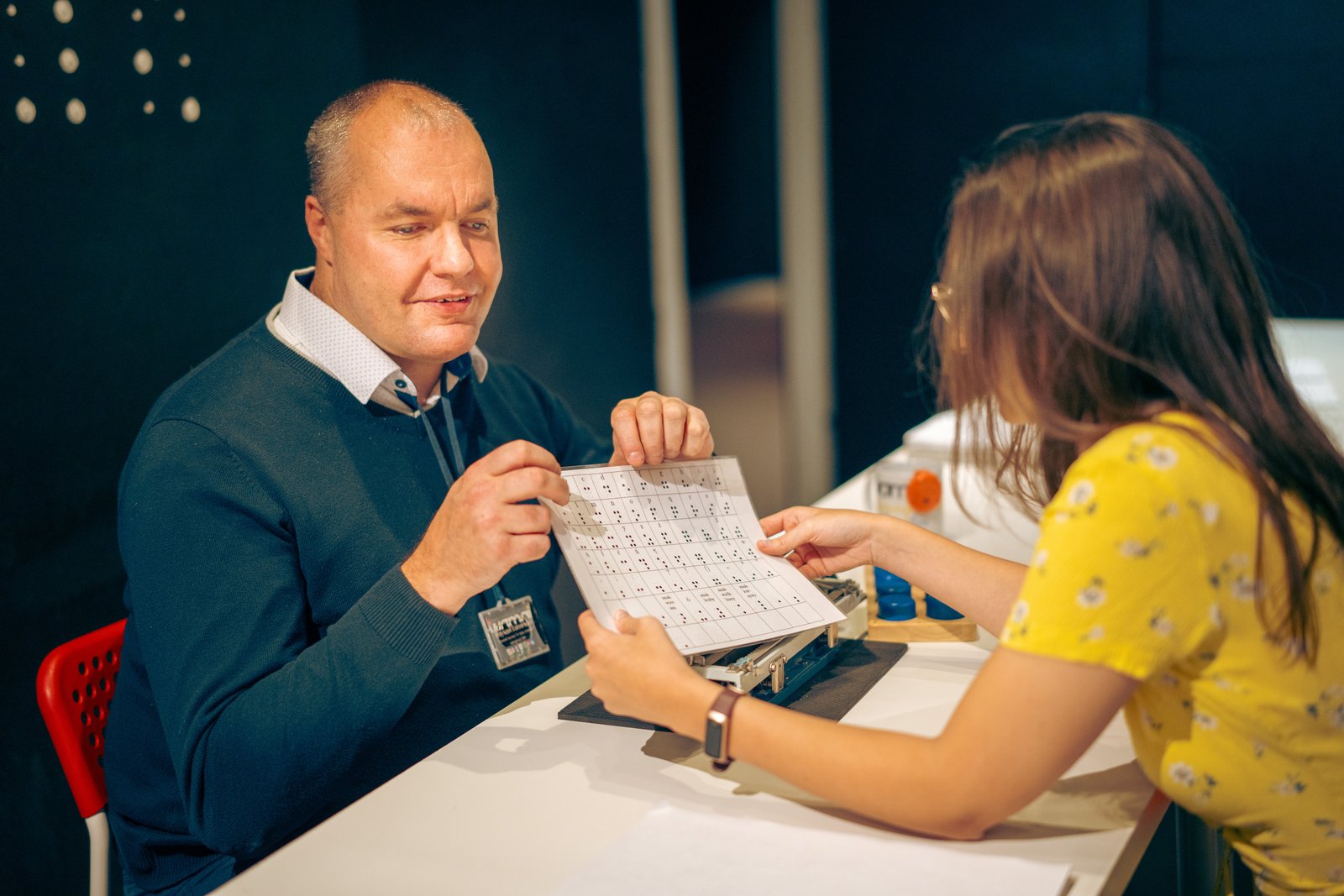 Przewodnik pokazuje zwiedzającej kartę z pismem Braille'a w Centrum Nauki i Zmysłów WOMAI w Krakowie